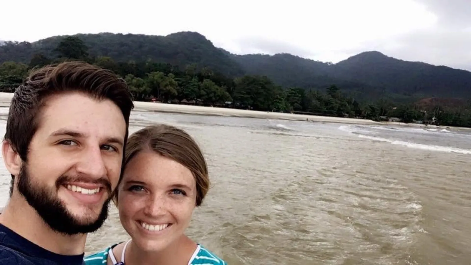 Michael and Chantelle on a beach with green mountains behind them in Sierra Leone