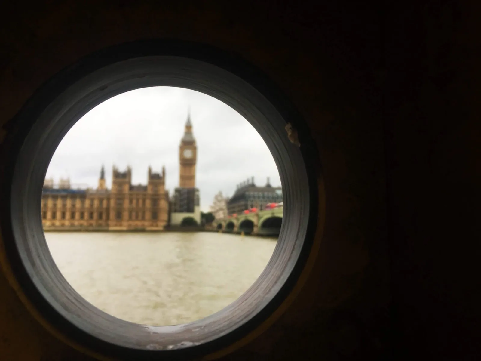Big Ben and the Houses of Parliament framed through a round window across the River Thames