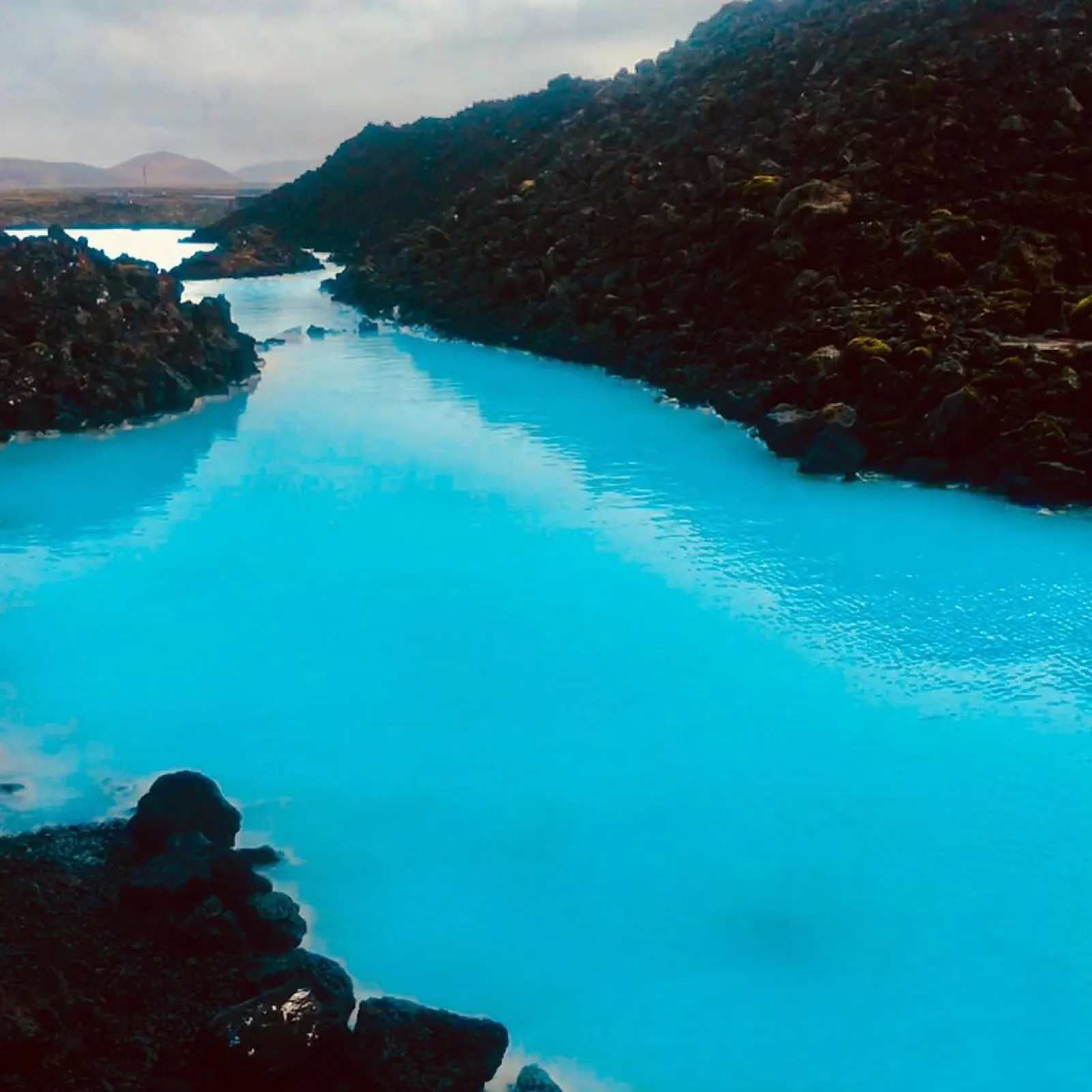 Bright milky-blue geothermal water between black lava rocks near the Blue Lagoon