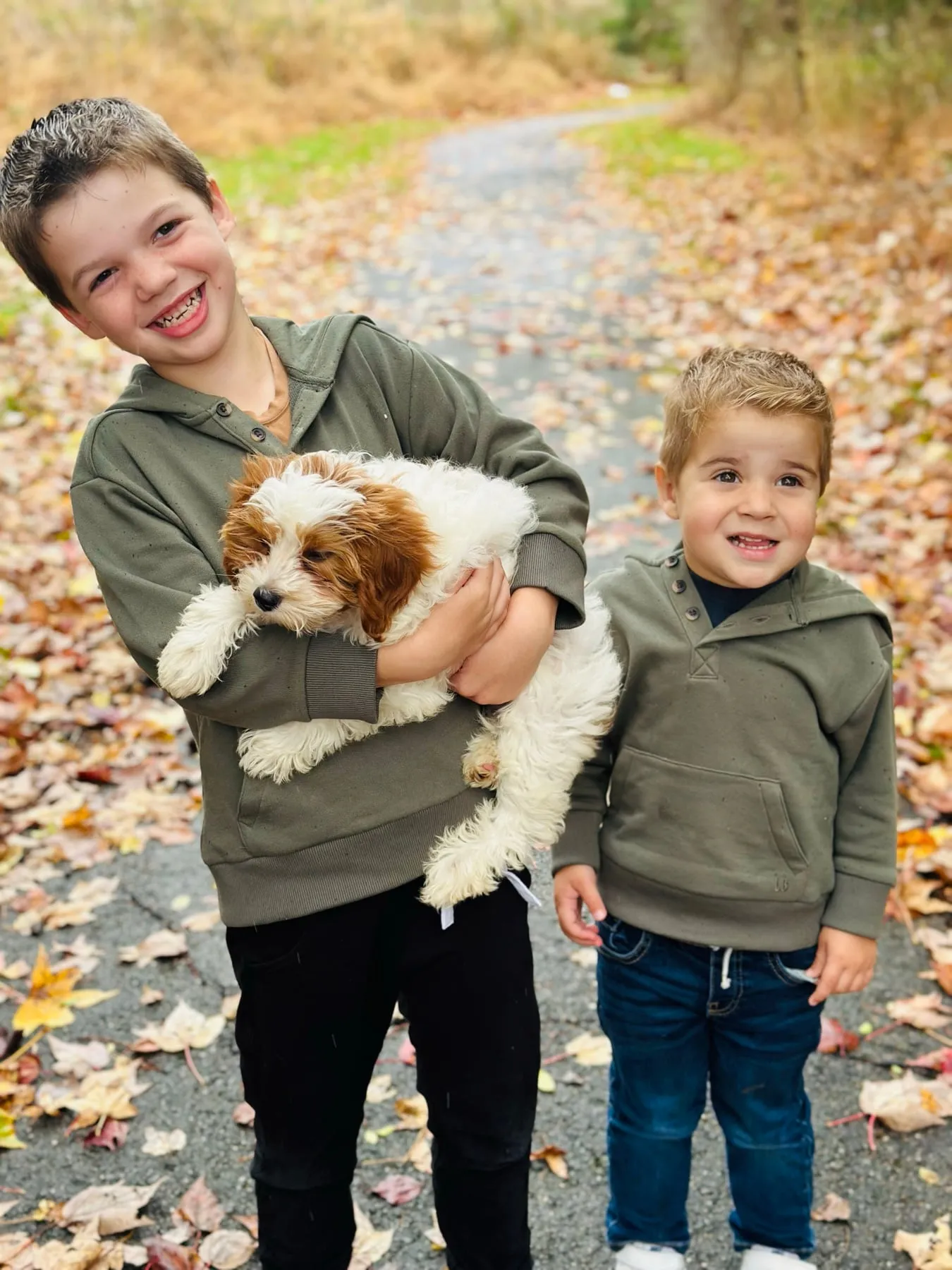 Our two boys holding our fluffy new puppy among fall leaves