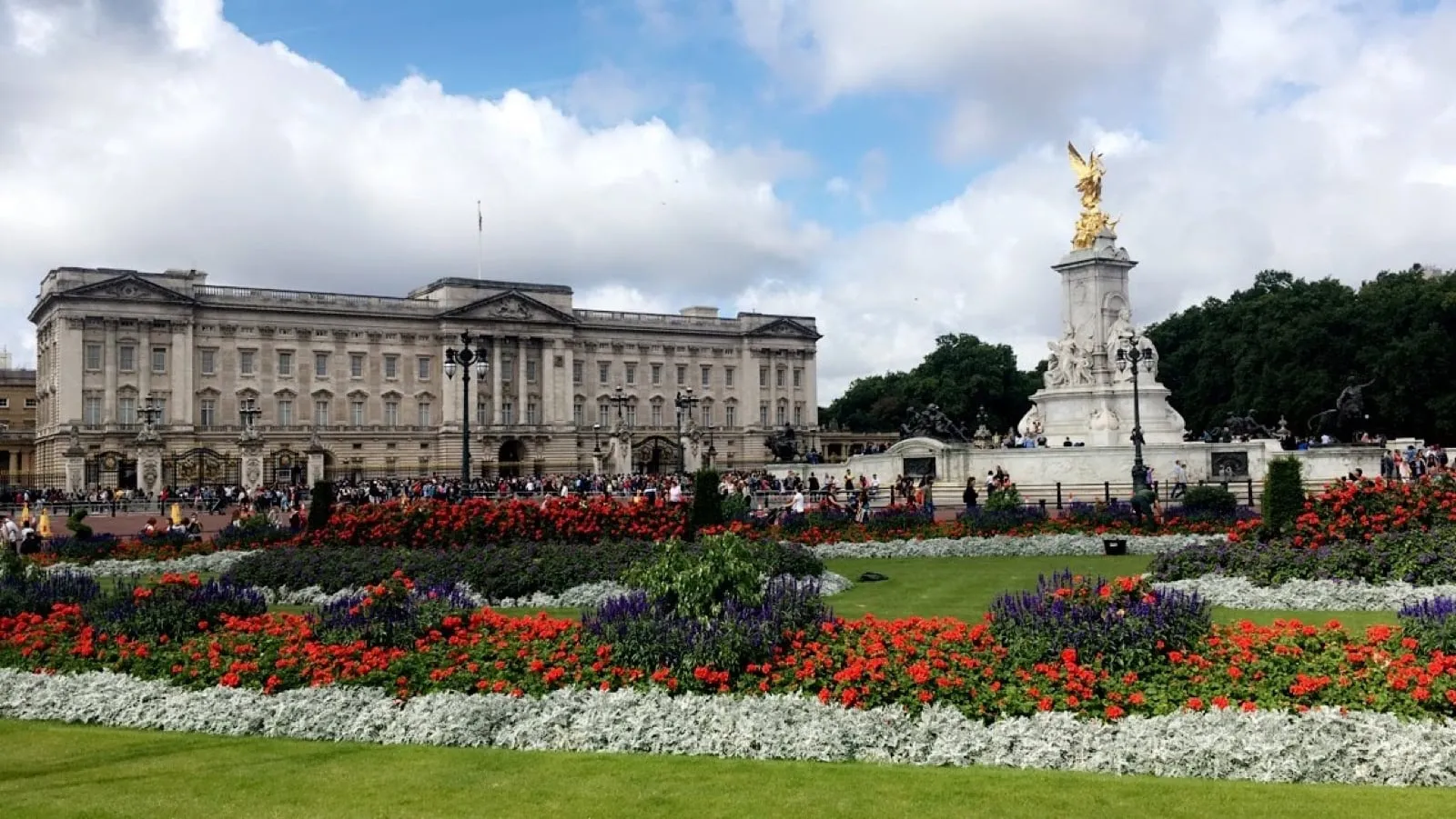 Buckingham Palace behind bright red and white flower beds, with the golden Victoria Memorial on the right