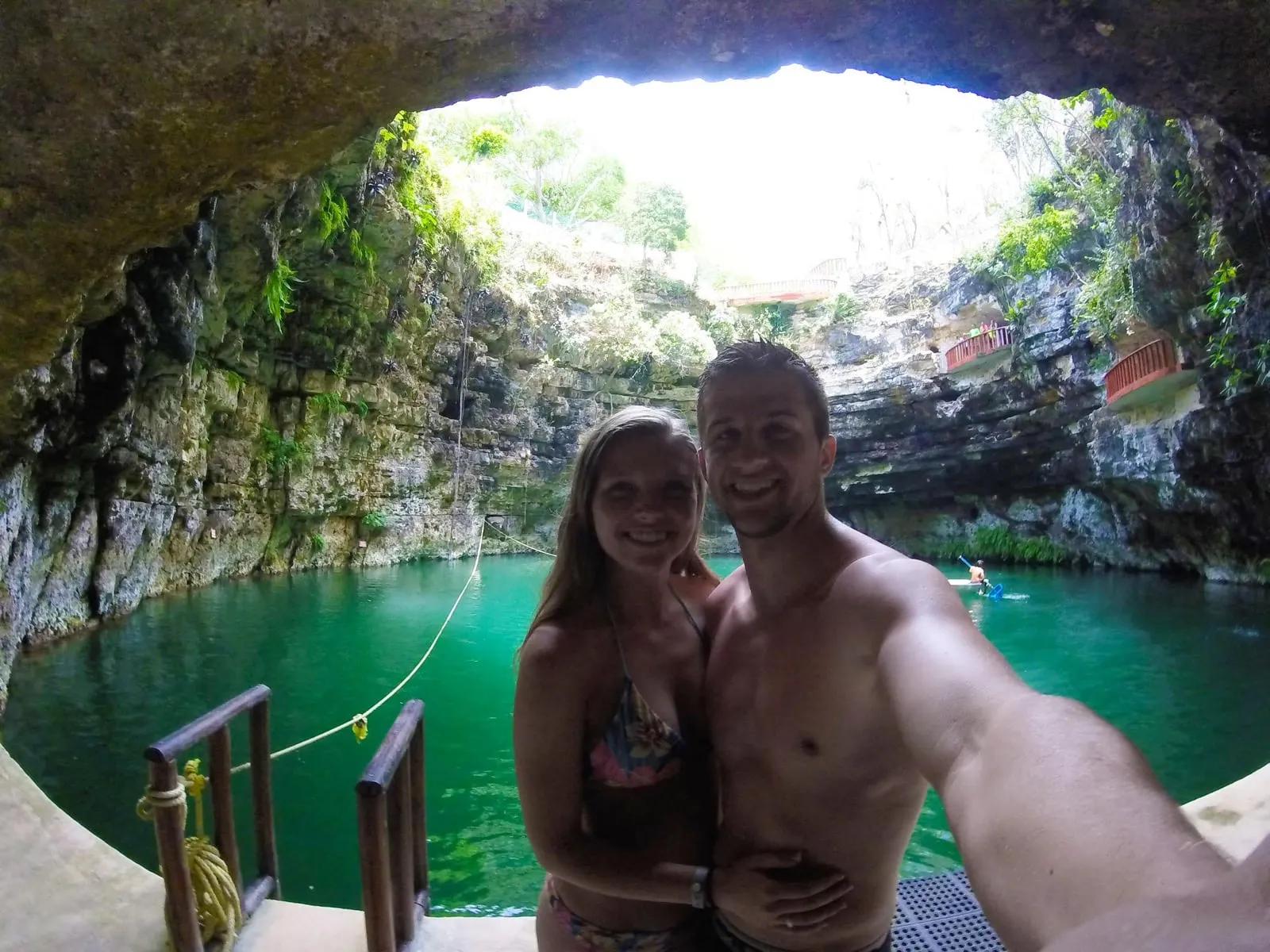 Michael and Chantelle taking a selfie inside a cenote, with green water and a round opening to the sky above them