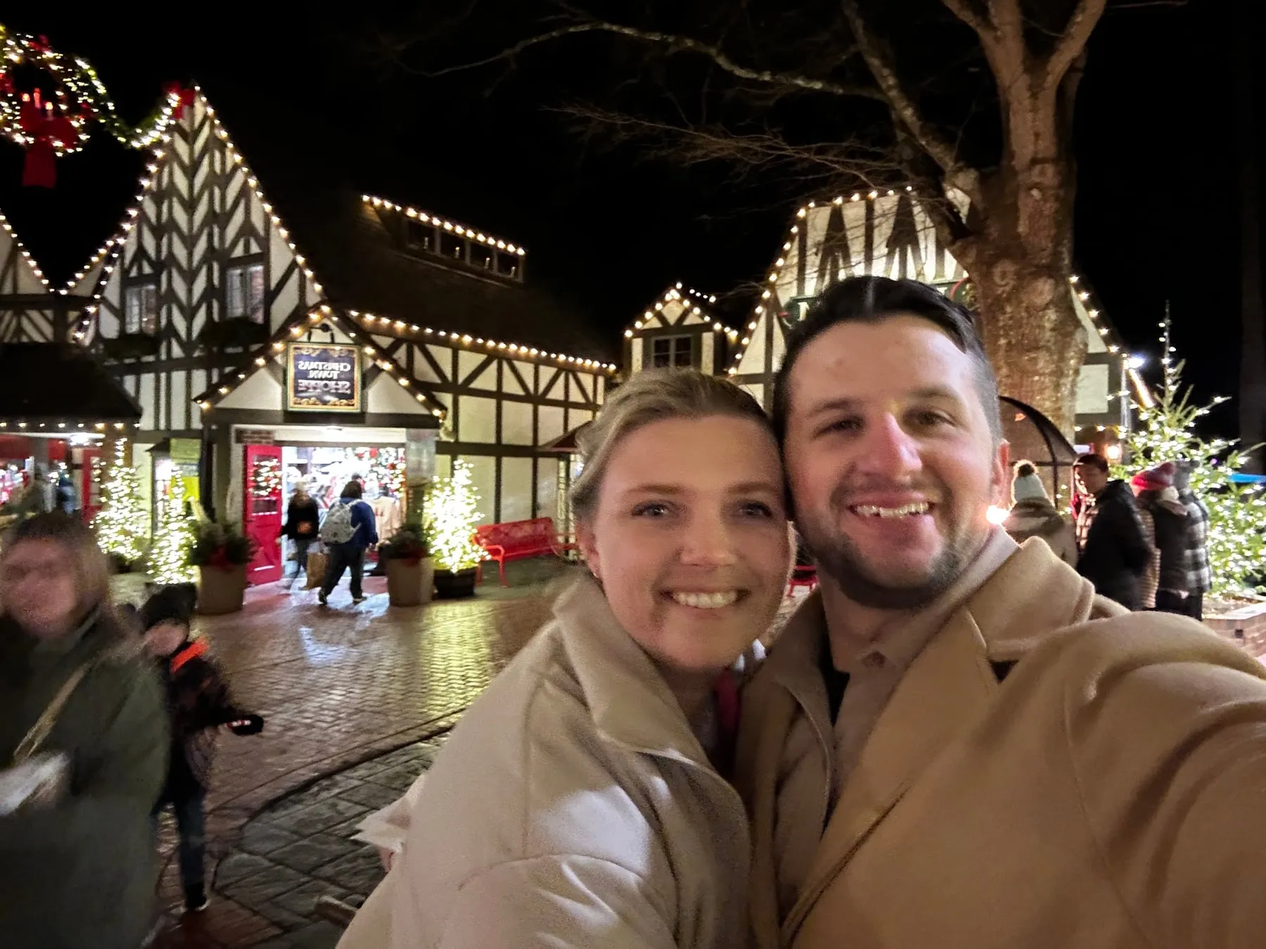 Michael and Chantelle taking a selfie in front of Christmas lights on Tudor-style buildings at night