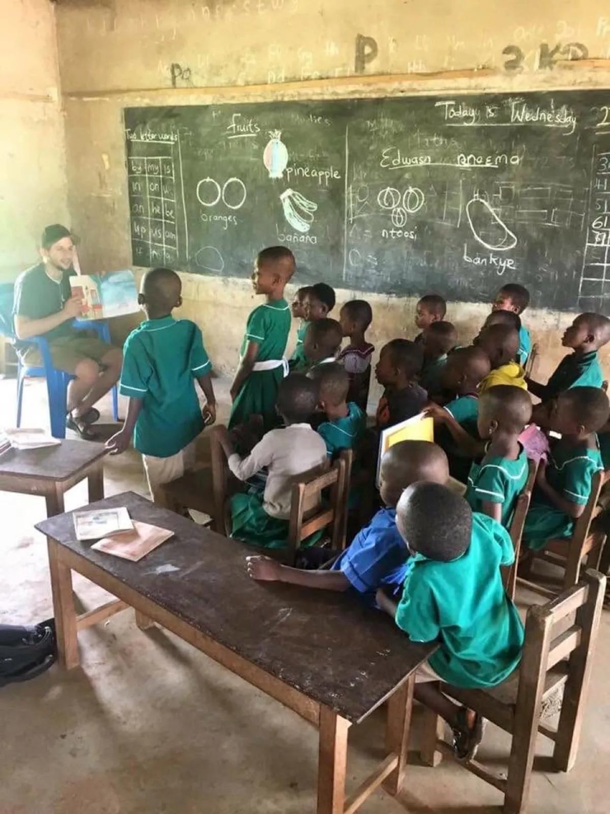 Michael teaching a classroom of students in green uniforms, with chalk drawings on the blackboard behind him