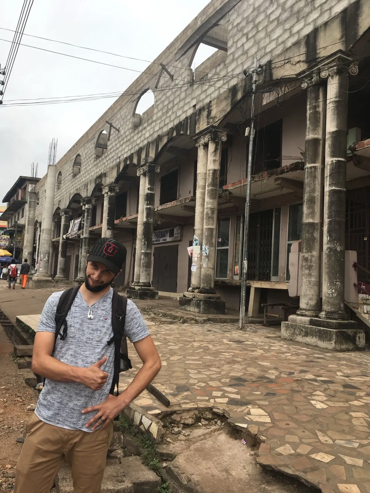 Michael standing on weathered cobblestone steps beside tall stone columns at Kakum National Park