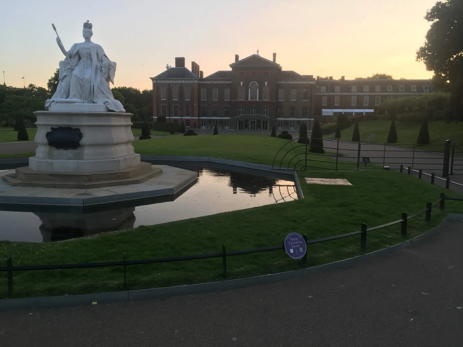Kensington Palace at dusk, with a white marble statue of Queen Victoria in front of it