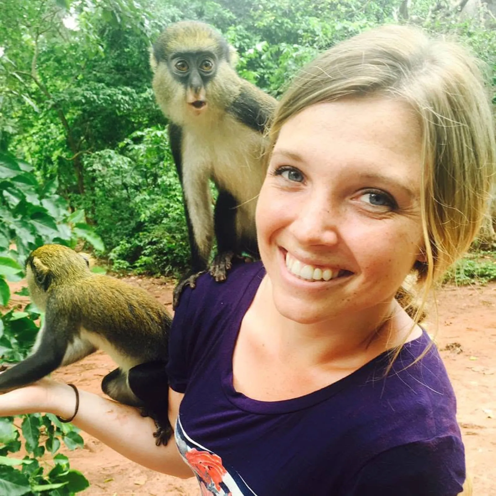 Chantelle smiling while two small monkeys climb on her shoulder and arm