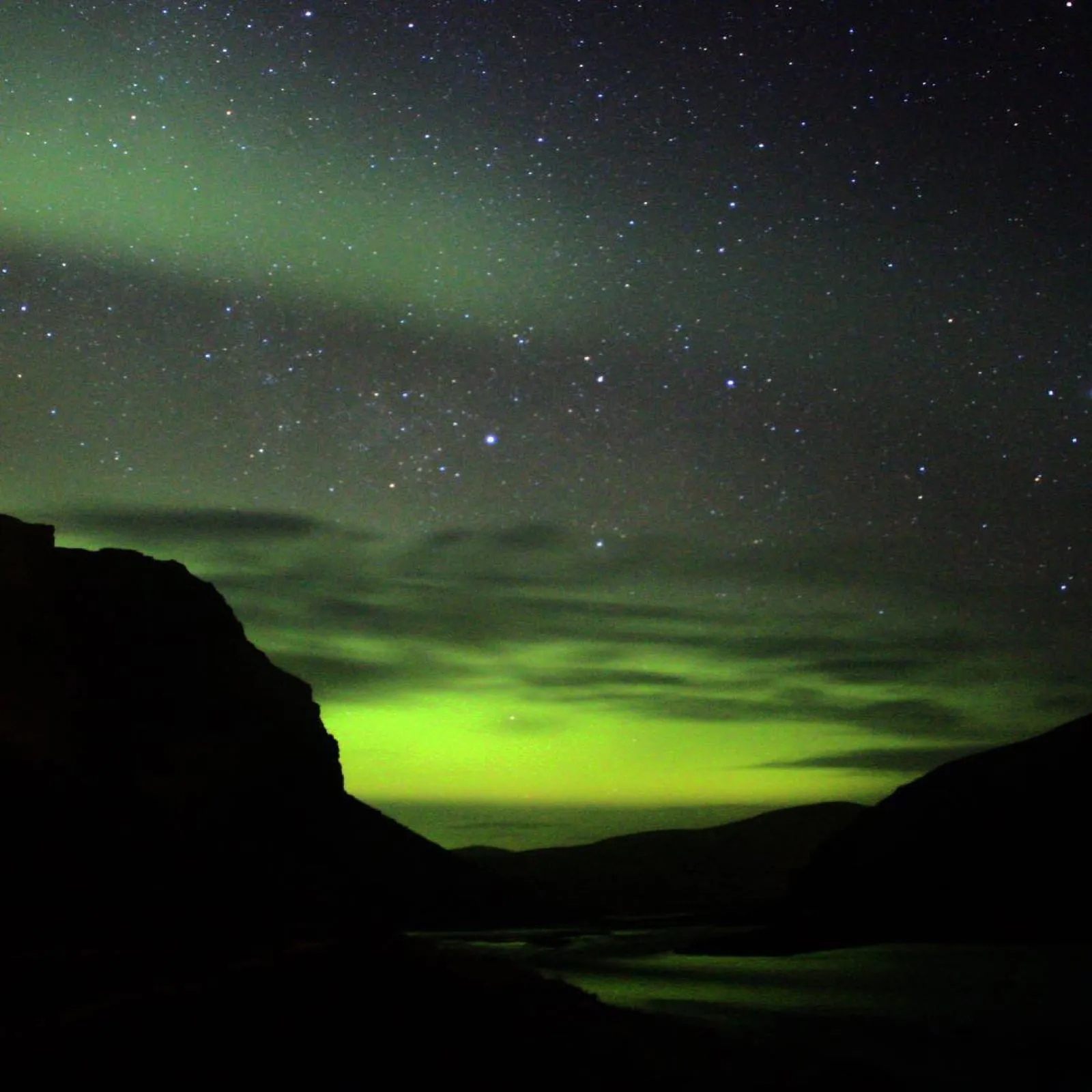 Bright green northern lights glowing over a dark mountain under a starry sky