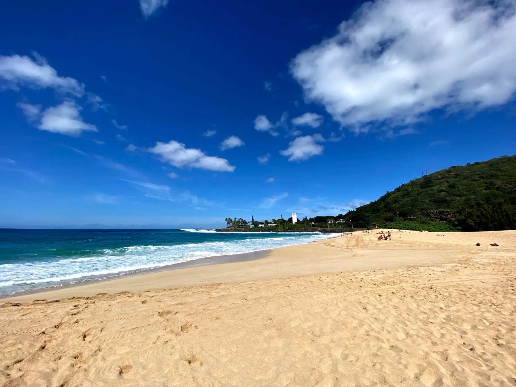 A golden Oahu beach under a bright blue sky with puffy white clouds