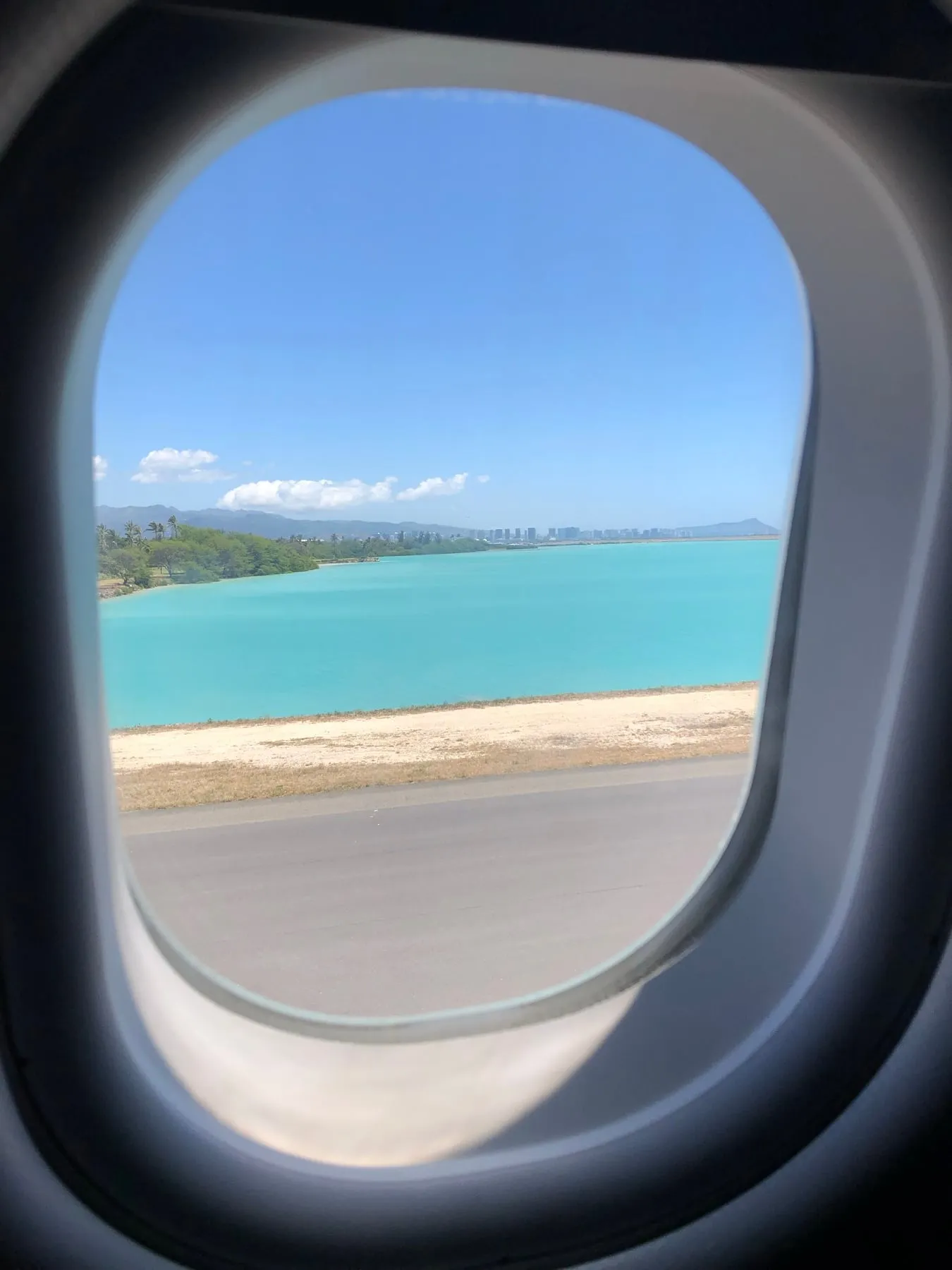 View from an airplane window of turquoise water and the Honolulu coastline while landing on Oahu