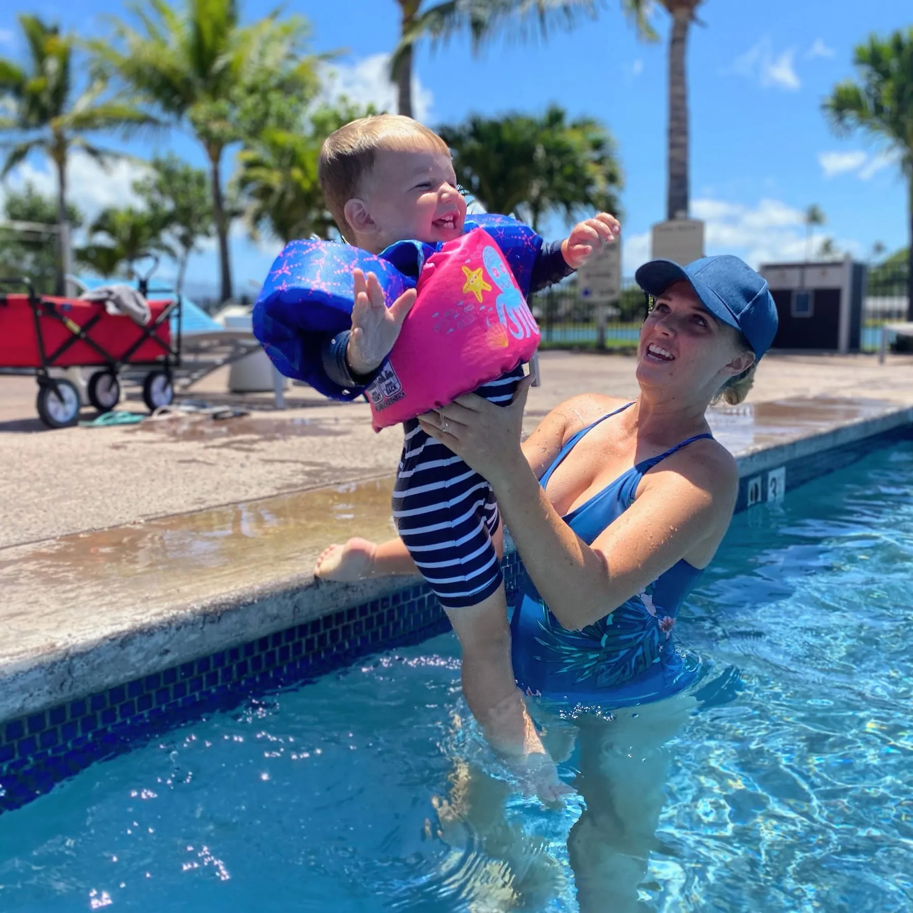 Chantelle lifting our baby, in a swim float vest, out of a pool on a sunny day in Hawaii