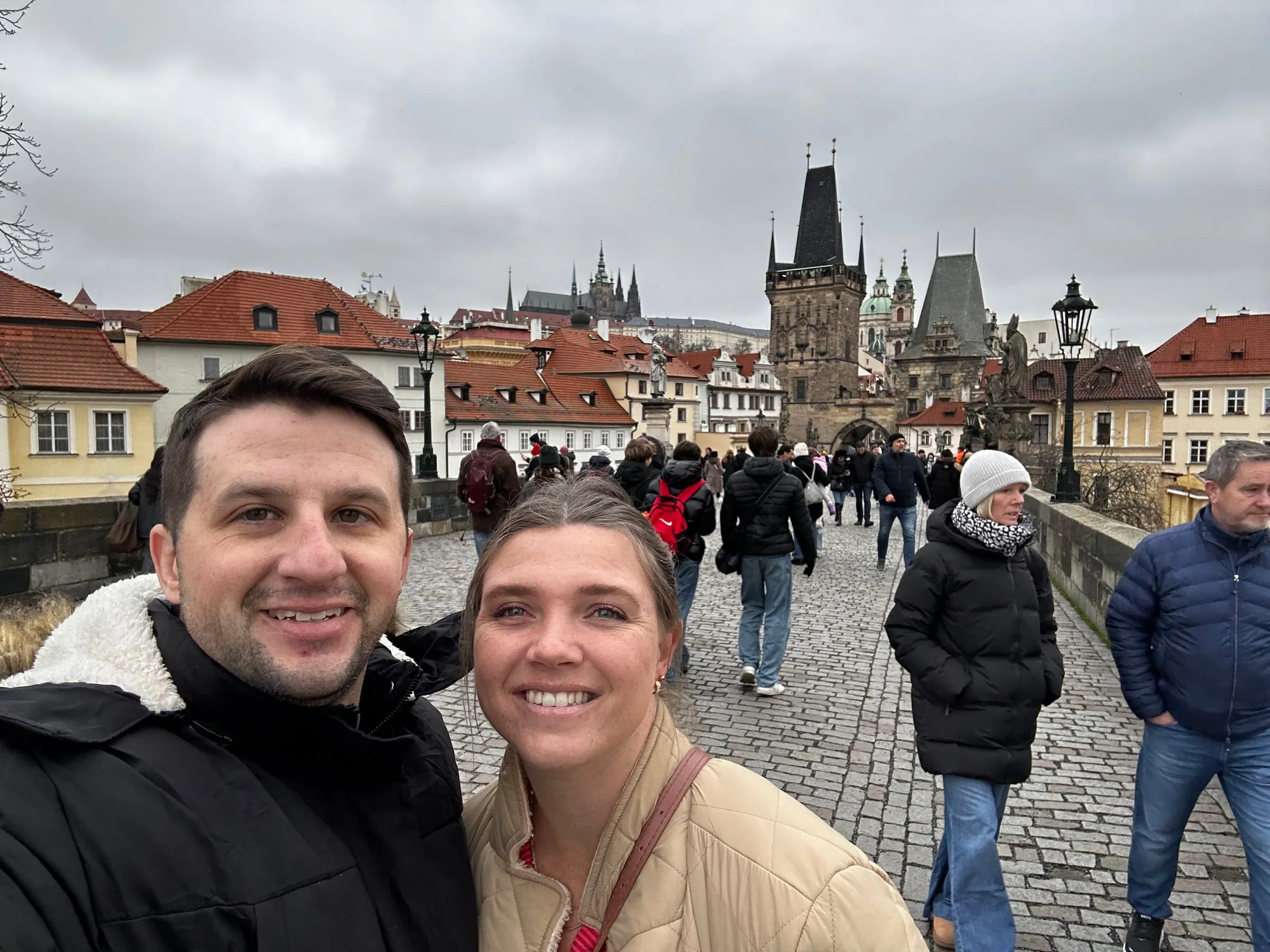 Michael and Chantelle taking a selfie on Charles Bridge with Prague's towers behind them