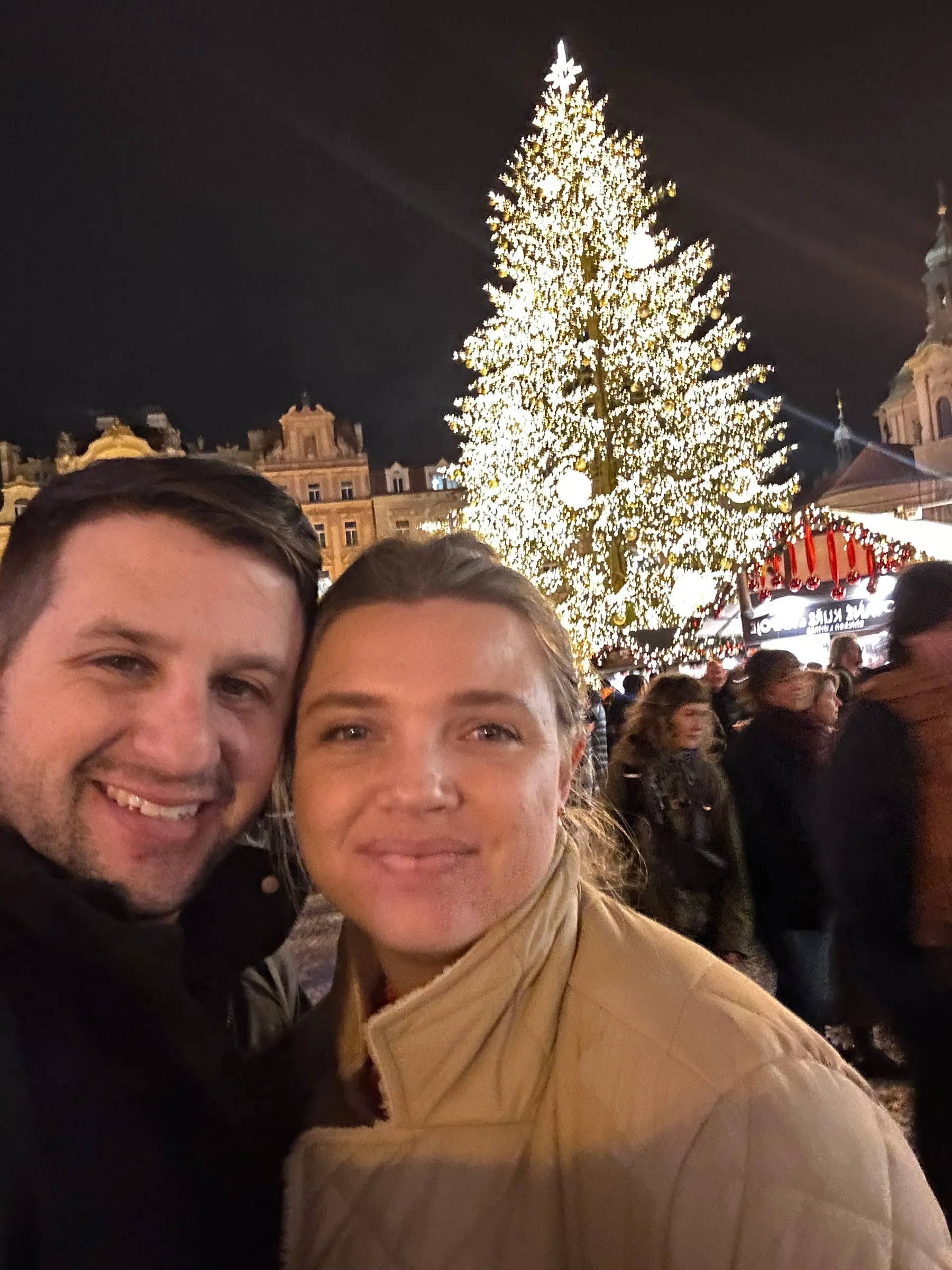 Michael and Chantelle taking a selfie in front of the Christmas tree and market stalls in Old Town Square