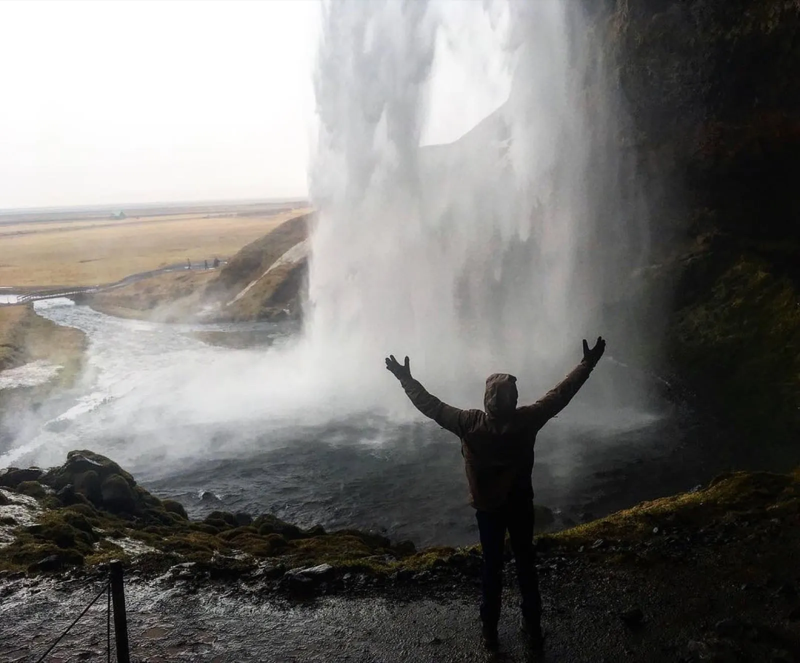 Michael with his arms raised behind the curtain of Seljalandsfoss waterfall