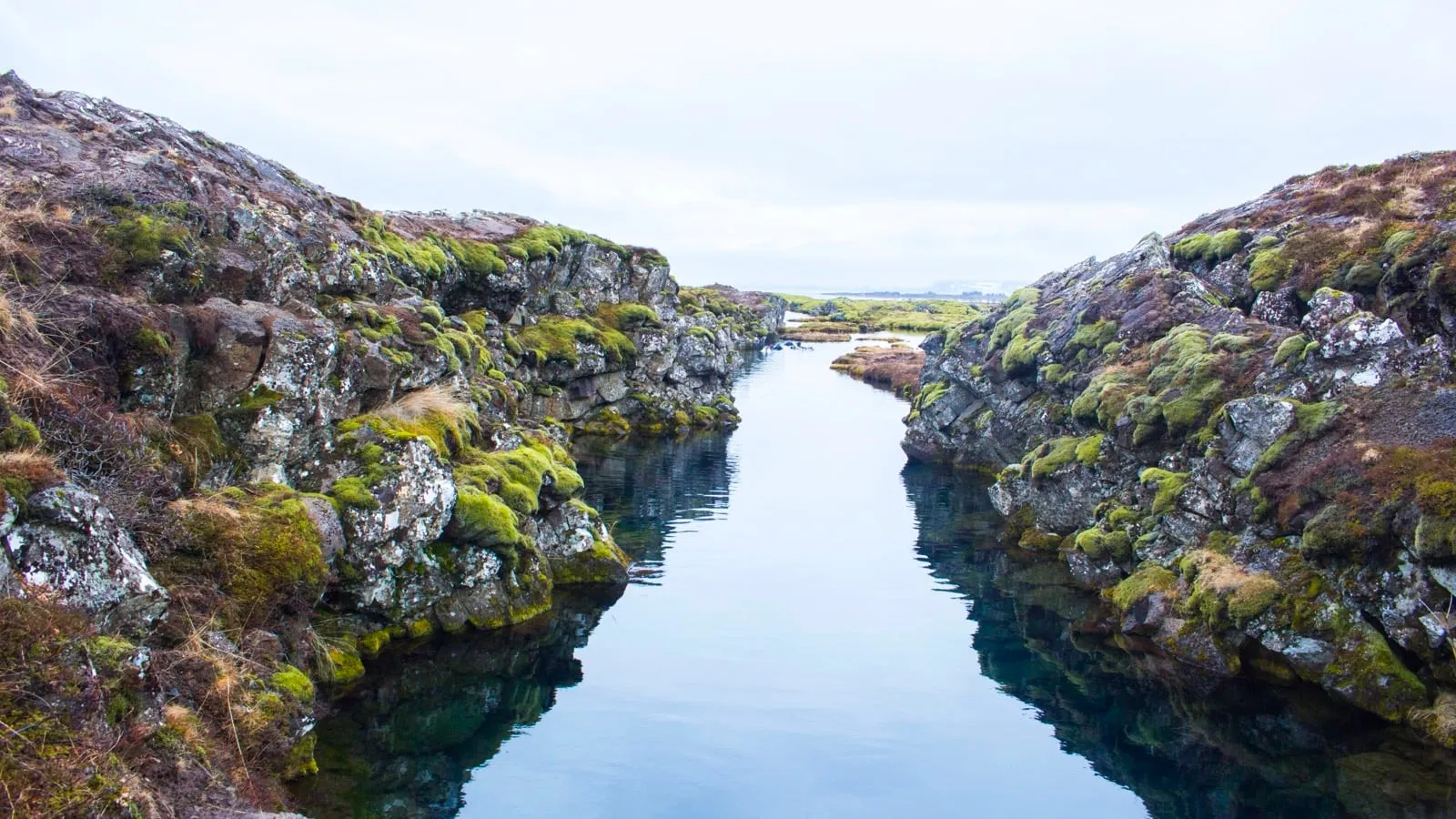 A narrow fissure of still, clear water between mossy lava rock walls at Þingvellir