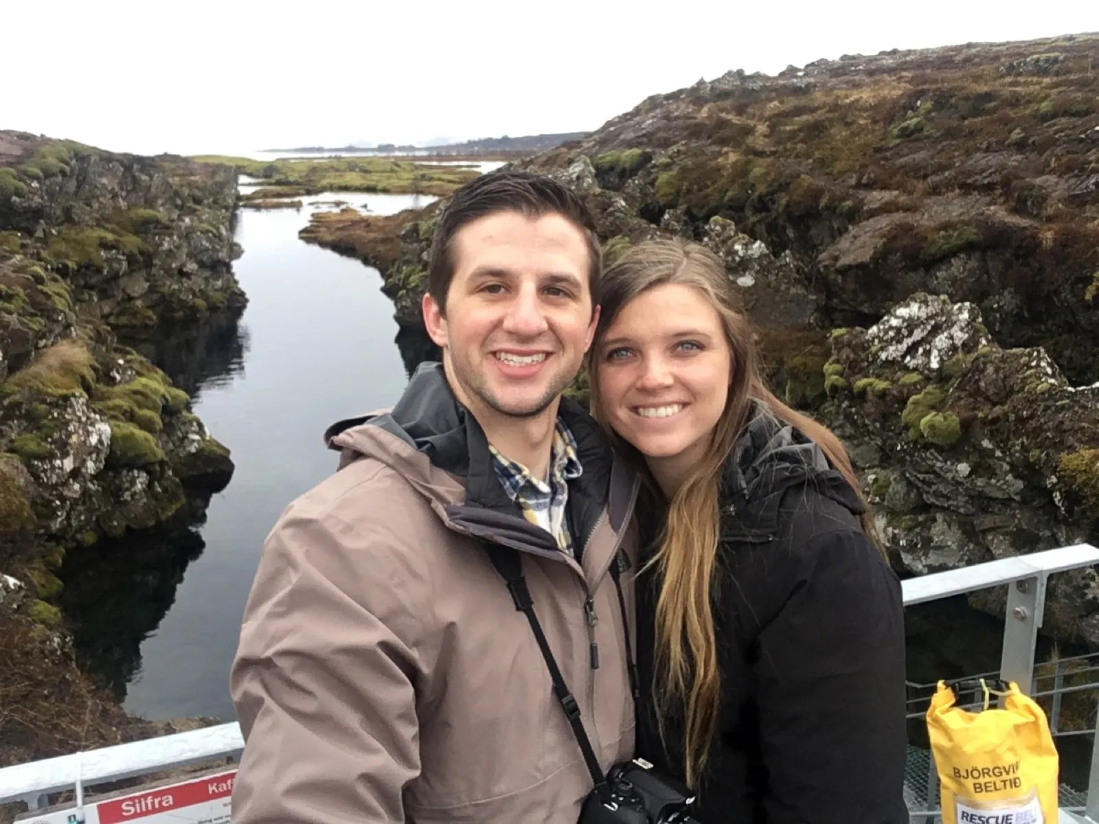 Michael and Chantelle smiling in front of a fissure filled with clear water at Þingvellir