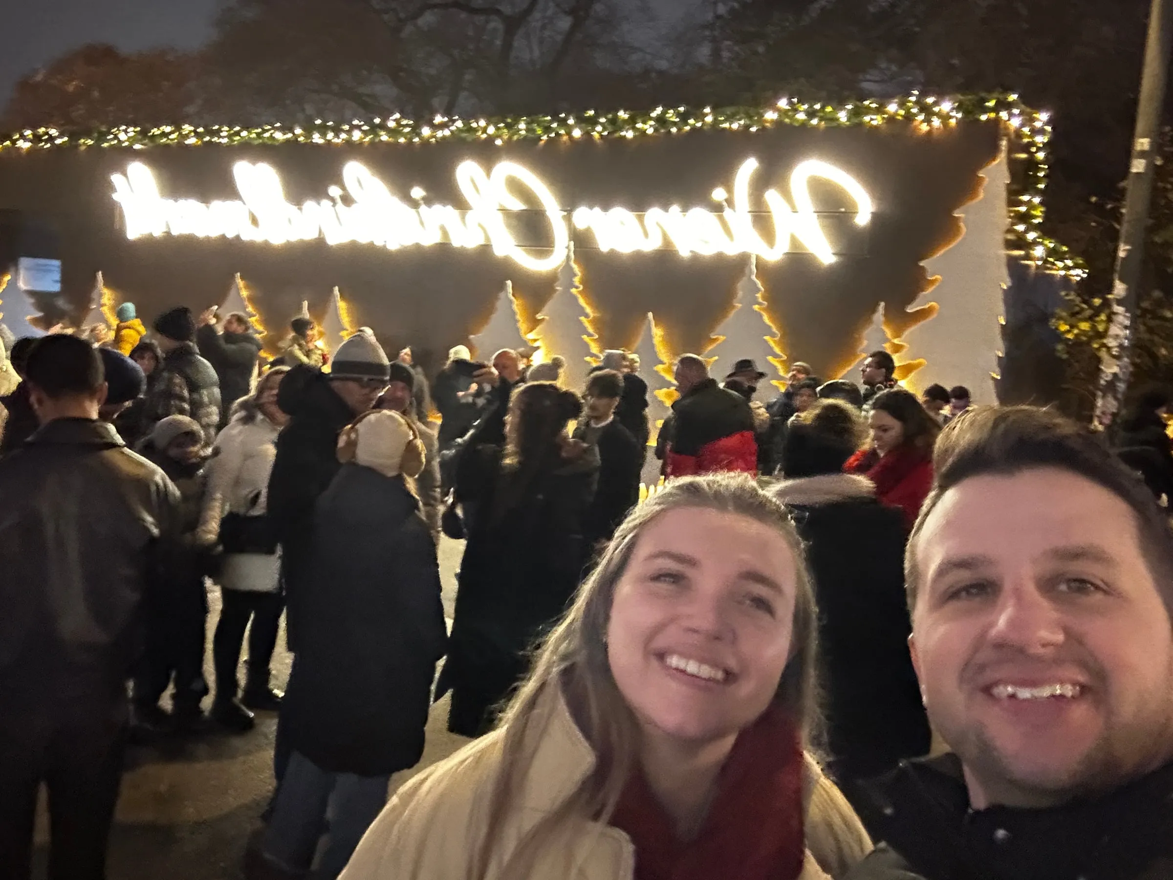 Michael and Chantelle smiling under the lit-up Wiener Christkindlmarkt sign