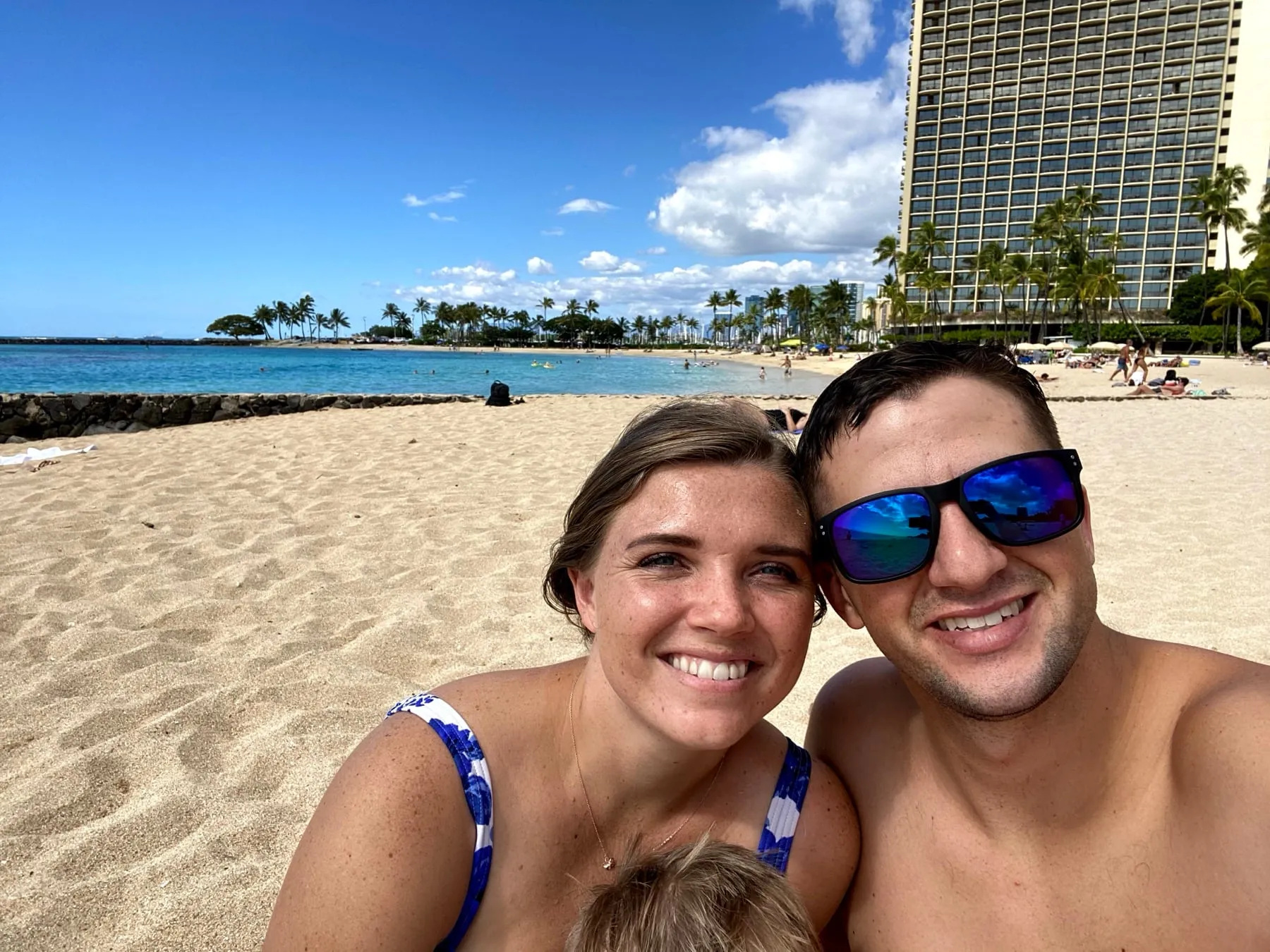 Michael and Chantelle smiling on a Waikiki beach with hotels and palm trees behind them