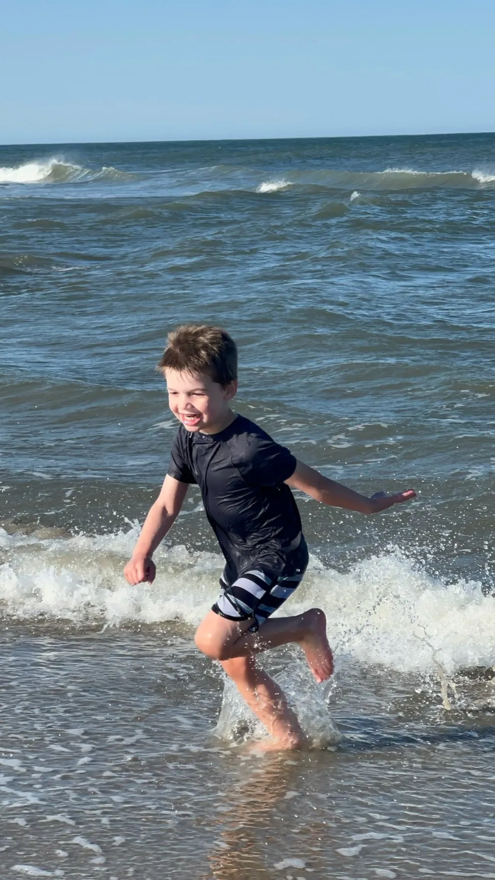 A boy laughing as he runs out of the waves